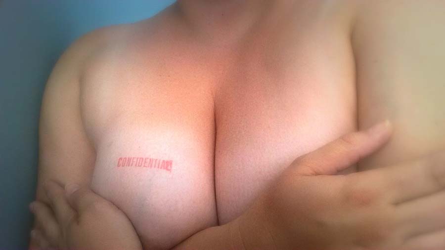A red stamp on the breast of woman that says "Confidential". Her arms are crossed over her breasts. Color.