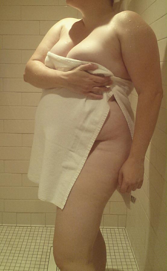 A woman holding a towel over her torso in the shower.