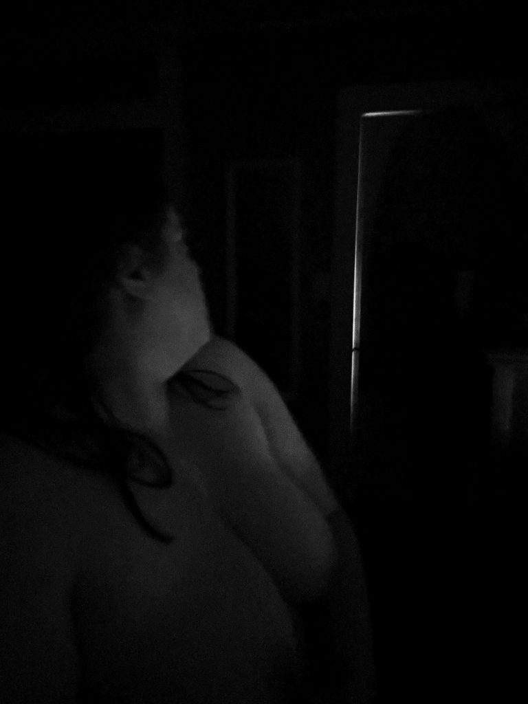 nude woman turns to face door in dark room