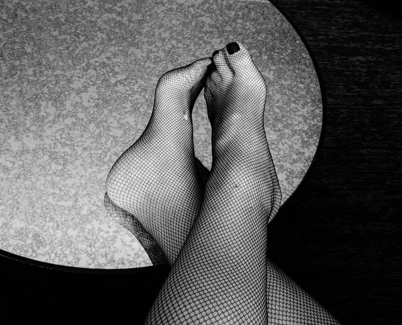 Black and white photo of ankles and feet in fishnets