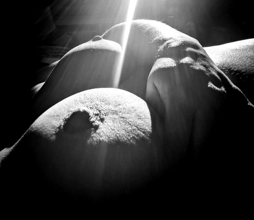 black and white photo, close up of breasts, ray of light appears to pierce one breast